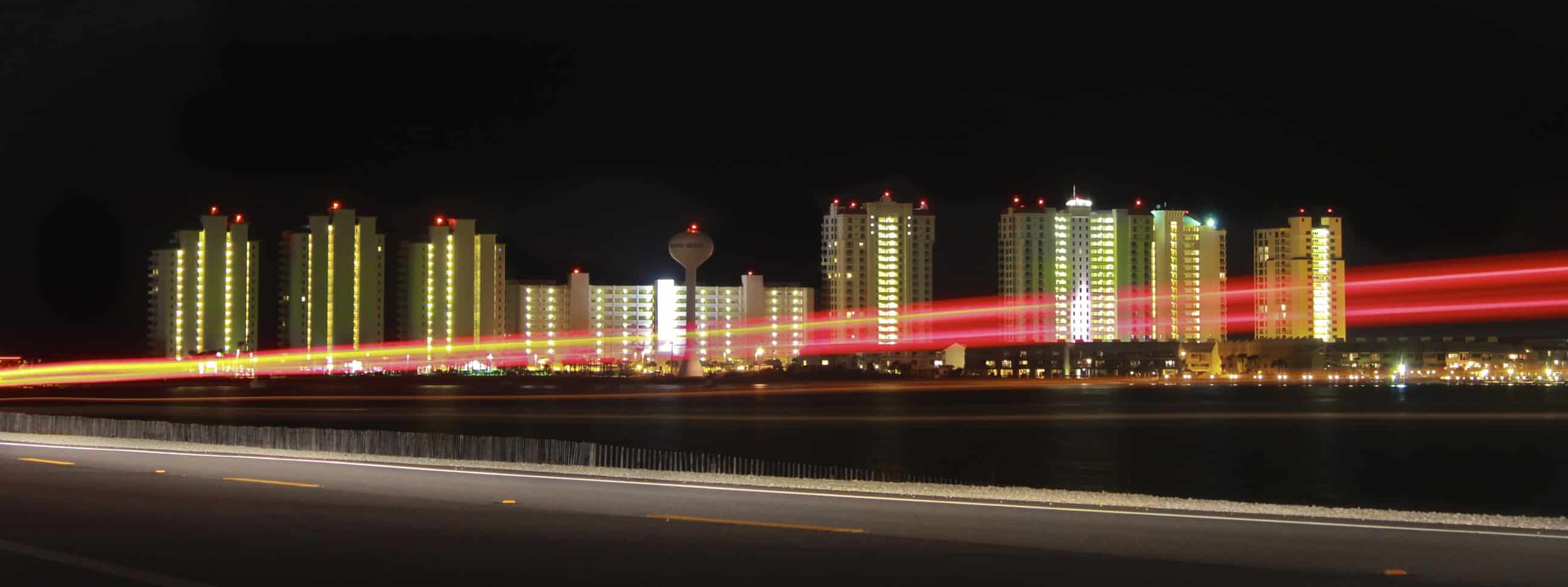 Navarre Beach condo towers lit at night beside a road with red and white light trails